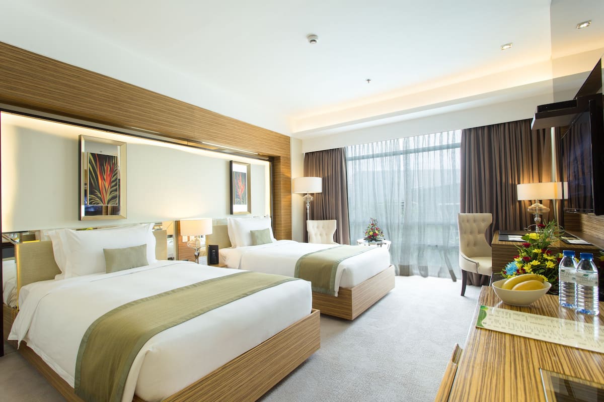 A hotel room with two beds, a dining table with a vase of flowers, and a large window with curtains.