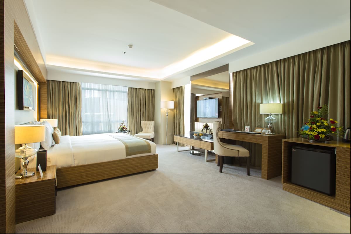 A hotel room with a large bed, a desk, a chair, a television, and a small refrigerator.
