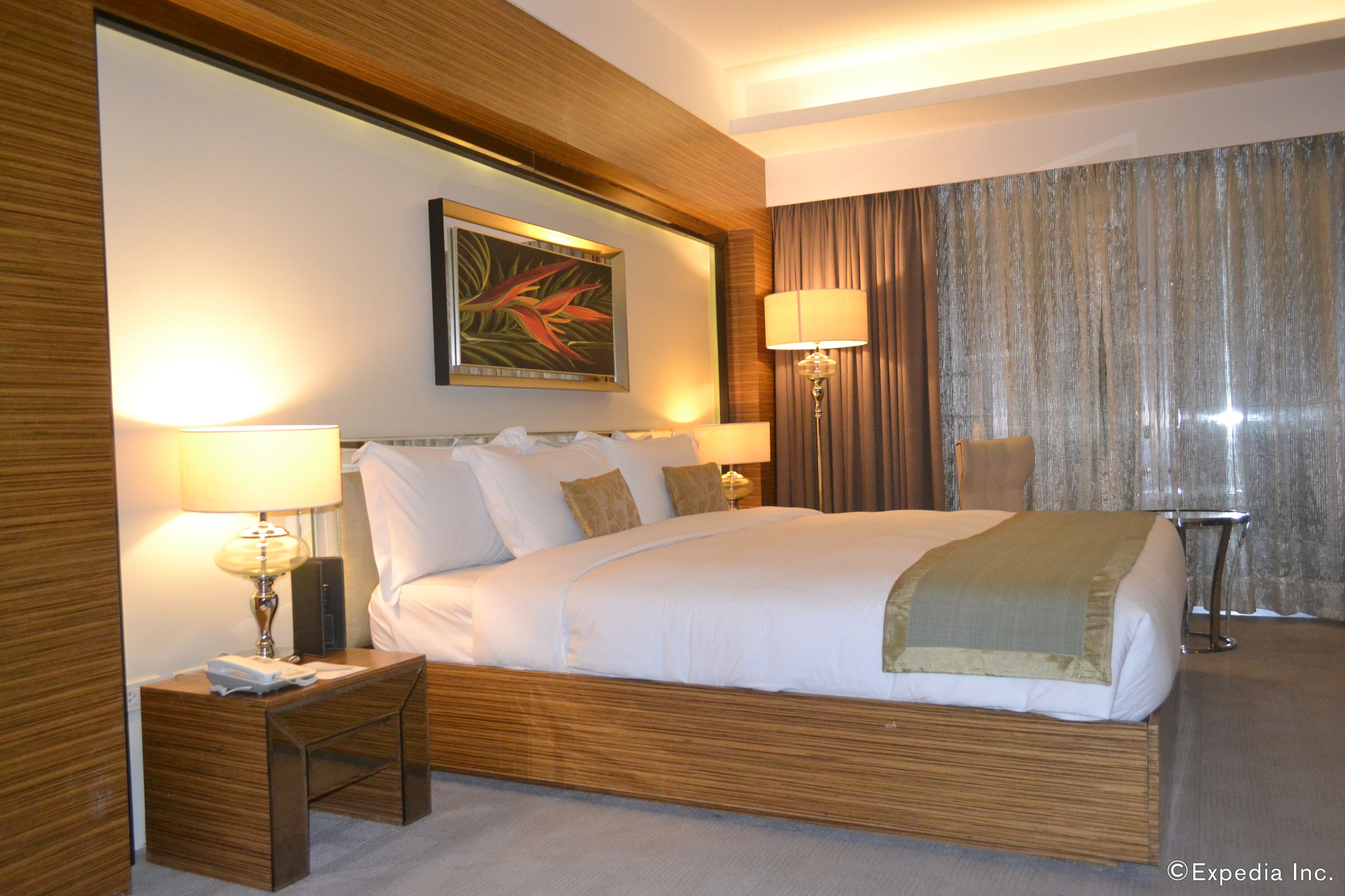 A hotel room with a large bed, two bedside tables, a nightstand, a lamp, a painting on the wall, and a curtain.