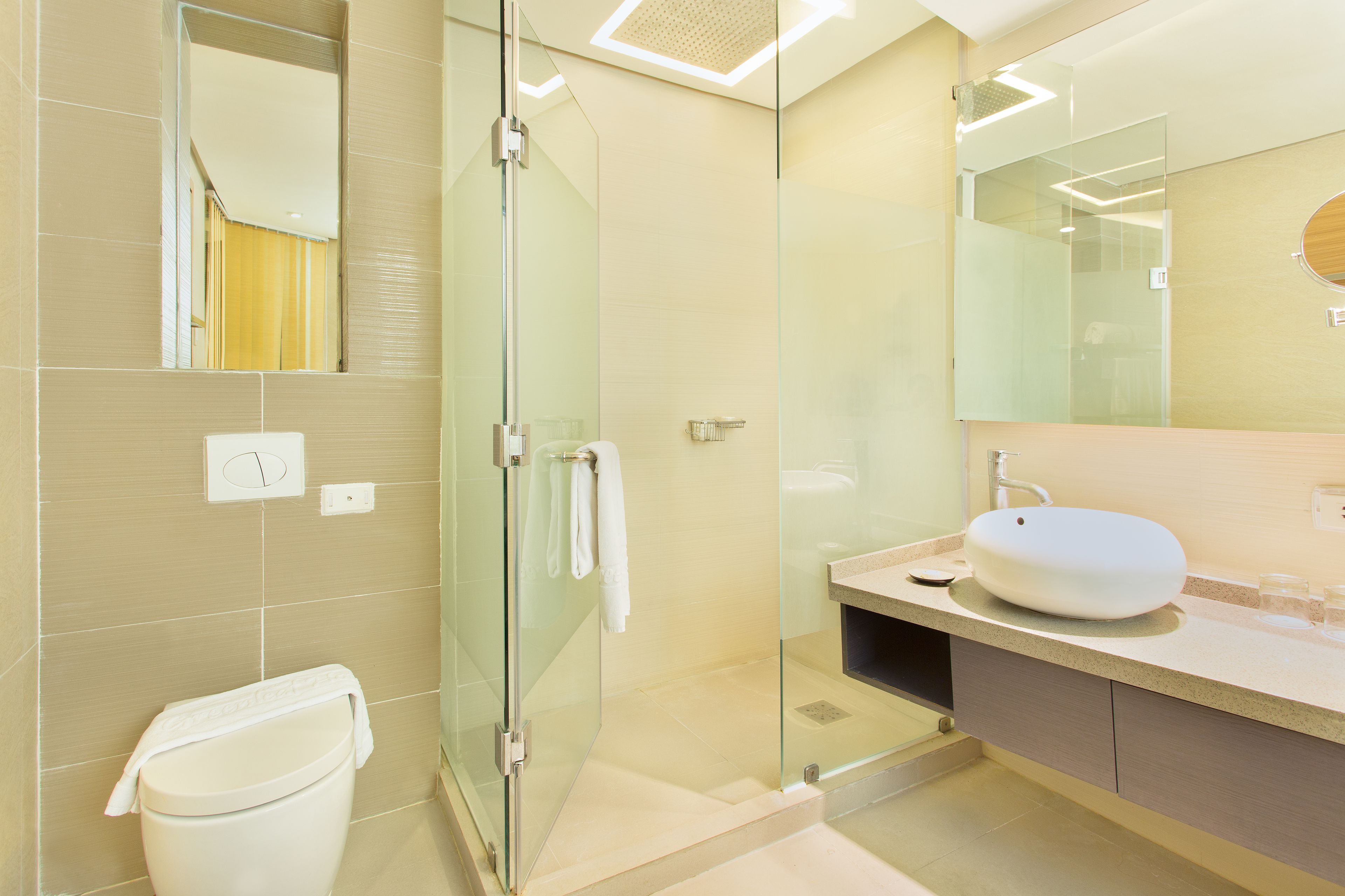 A modern bathroom with a glass-enclosed shower, a white toilet, and a beige sink with a round mirror above it.