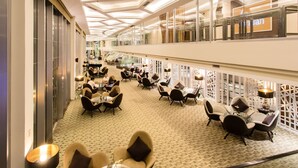Un amplio vestíbulo de hotel con varias zonas de estar, un techo alto con iluminación moderna y vistas del interior a través de grandes ventanales.