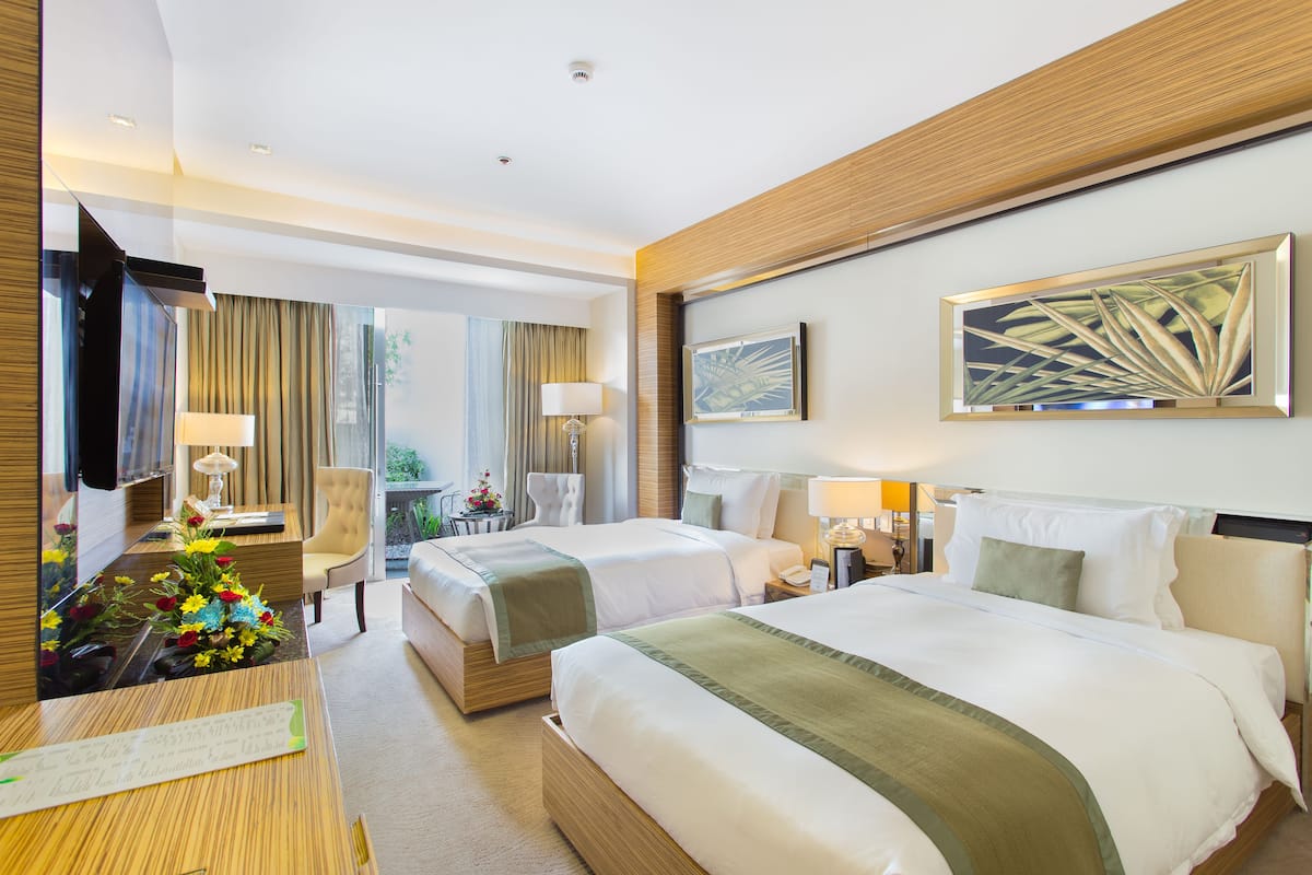 A hotel room with two beds, a desk with a lamp, a TV, and a large window with curtains.