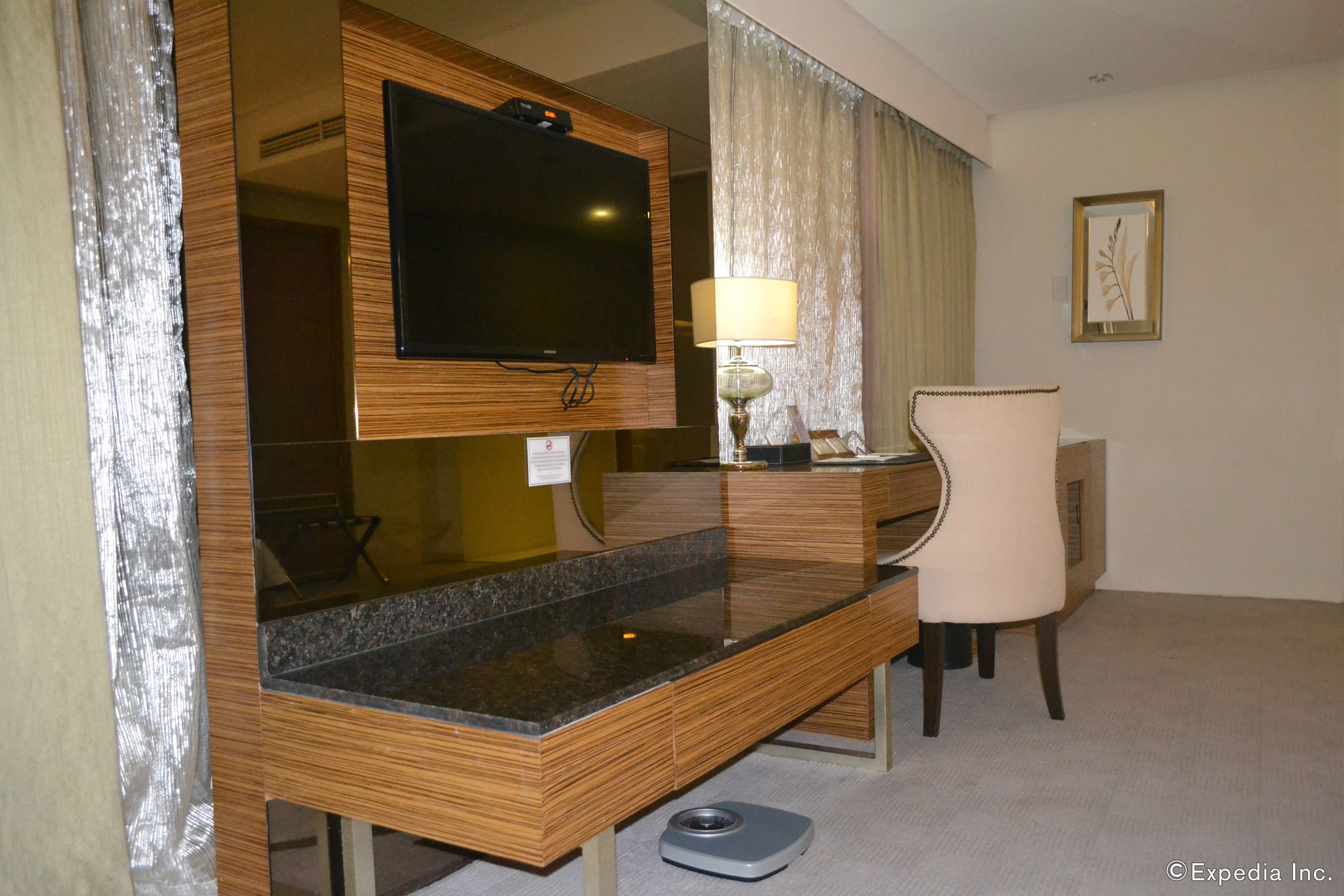 Habitación de hotel con tocador de madera, televisor de pantalla plana, lámpara, silla y balanza.