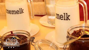 Três milkshakes com a palavra 'melk' escrita nelas, um pote de vidro com uma colher e o logotipo do Stadshotel Ootmarsum.