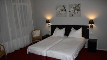 A double bed with white linens, two wall-mounted lamps, and two abstract floral paintings on the wall.