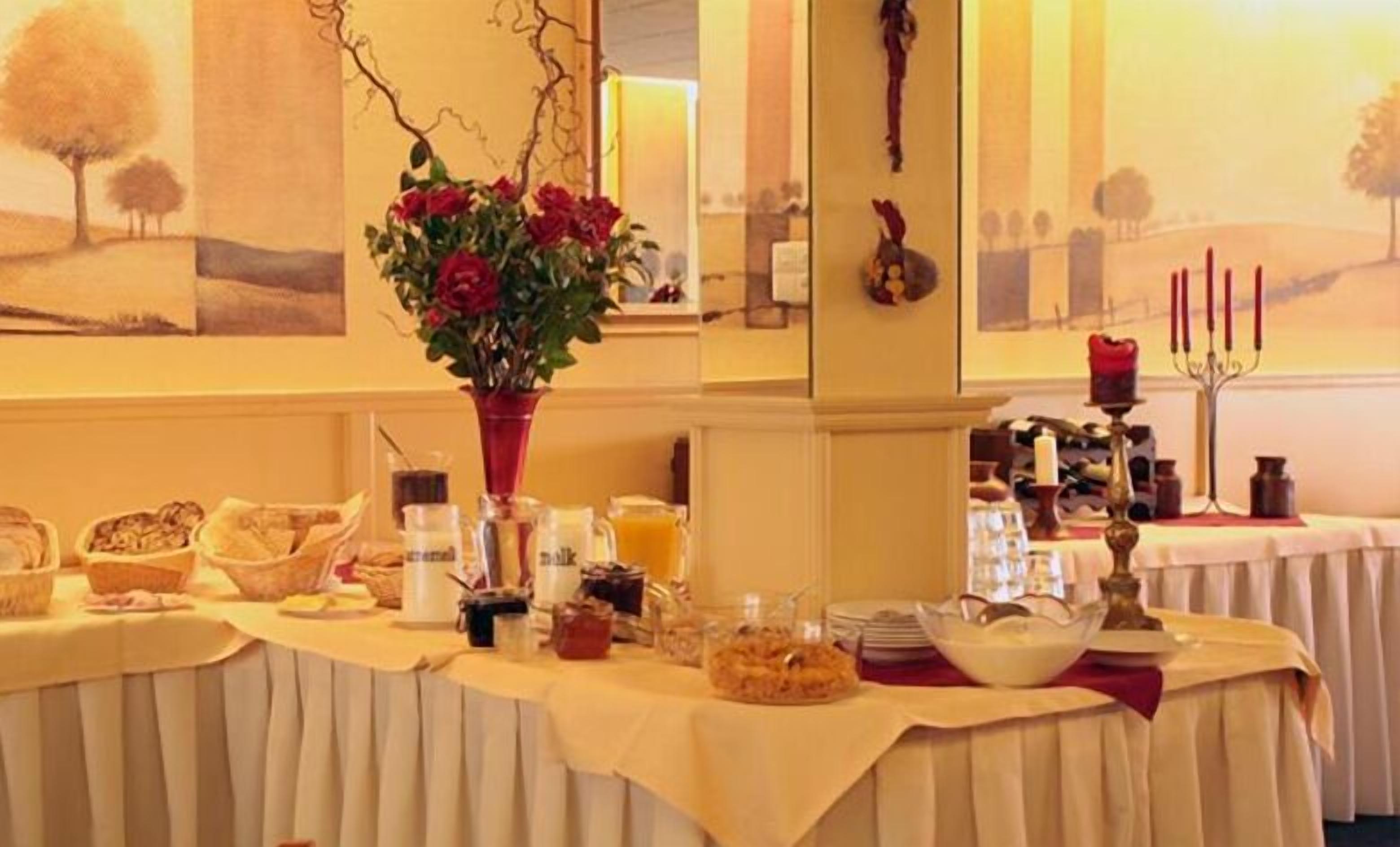 A buffet table with various food items and a vase of red roses.