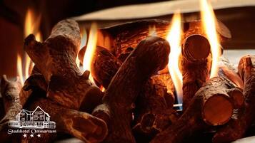 A fireplace with logs burning, a candle holder, and a logo for Stadshotel Ootmarsum.