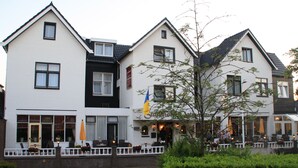 Un bâtiment à deux étages, doté d’une façade blanche et d’un toit noir. Un drapeau est accroché au bâtiment, et un arbre se trouve devant.