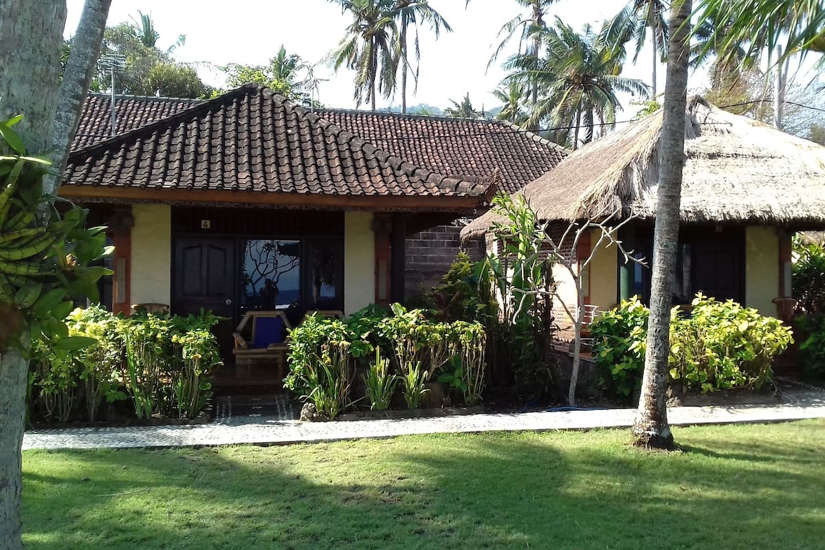 A traditional building with a tiled roof and thatched roof structures, surrounded by lush greenery and palm trees.
