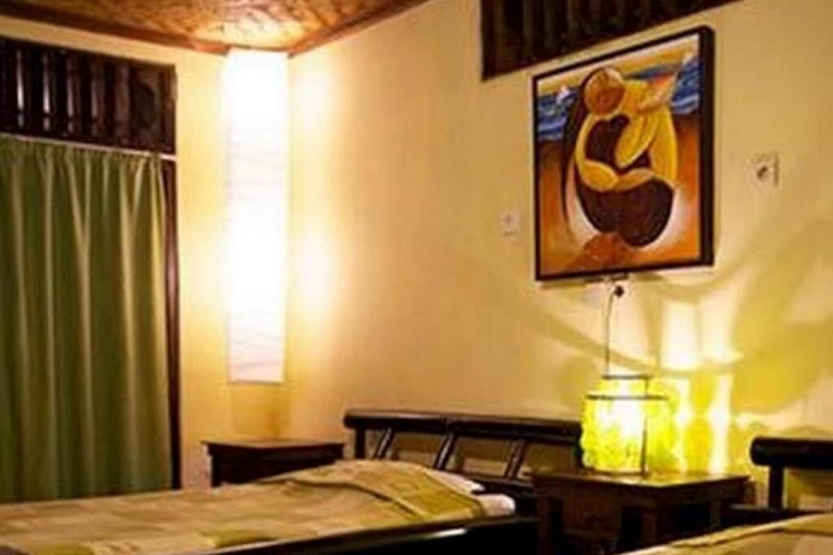 A room with a bed, a nightstand, a lamp, a painting on the wall, and a window with curtains.