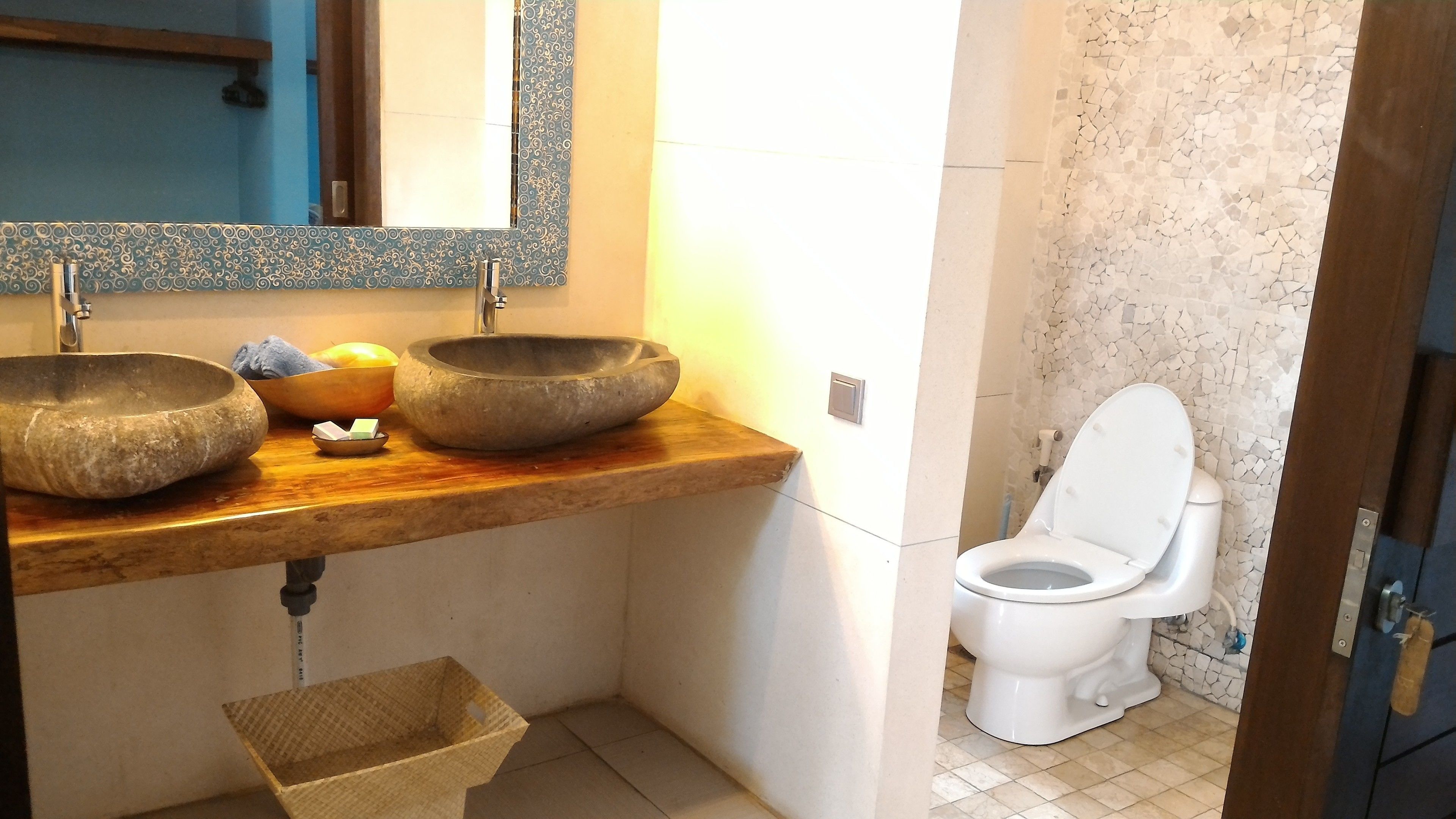 A bathroom with two stone sinks, a wooden vanity, a white toilet, and a mirror above the sinks.