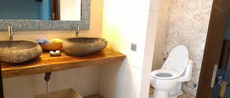 Un baño con dos lavamanos de piedra, un mueble de tocador de madera, un inodoro blanco y un espejo sobre los lavamanos.