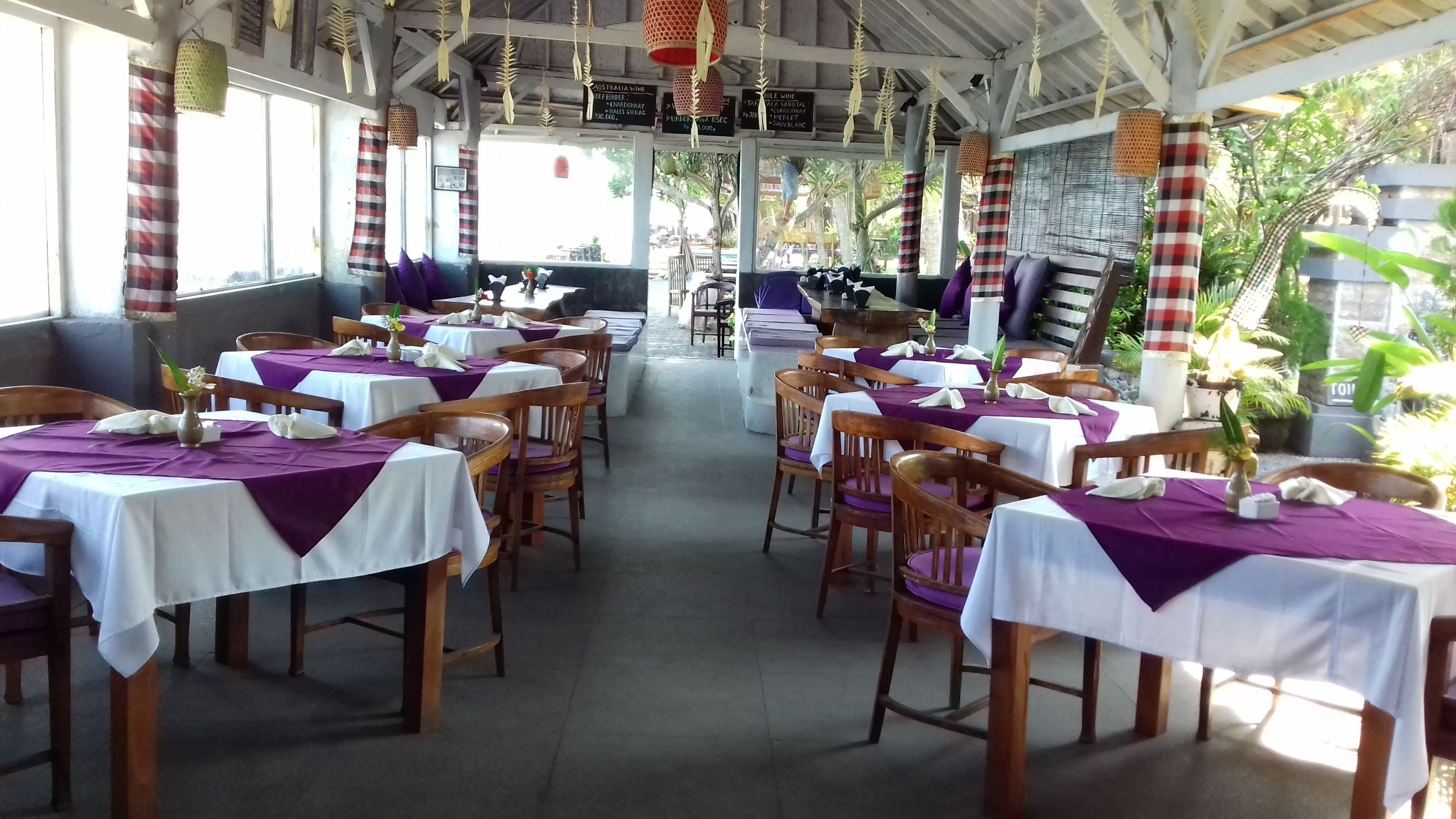 A restaurant with tables covered in white and purple tablecloths, wooden chairs, and hanging decorations.