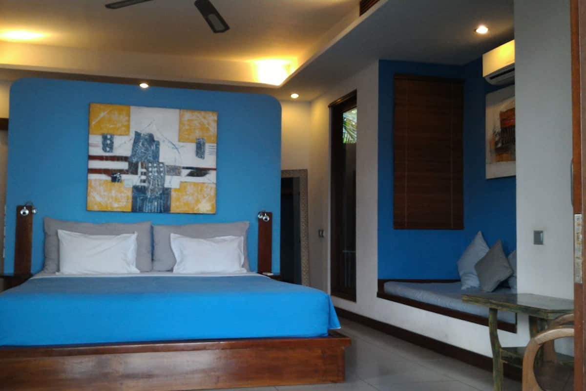 A bedroom with a bed, a ceiling fan, a wall with a painting, and a window with blinds.