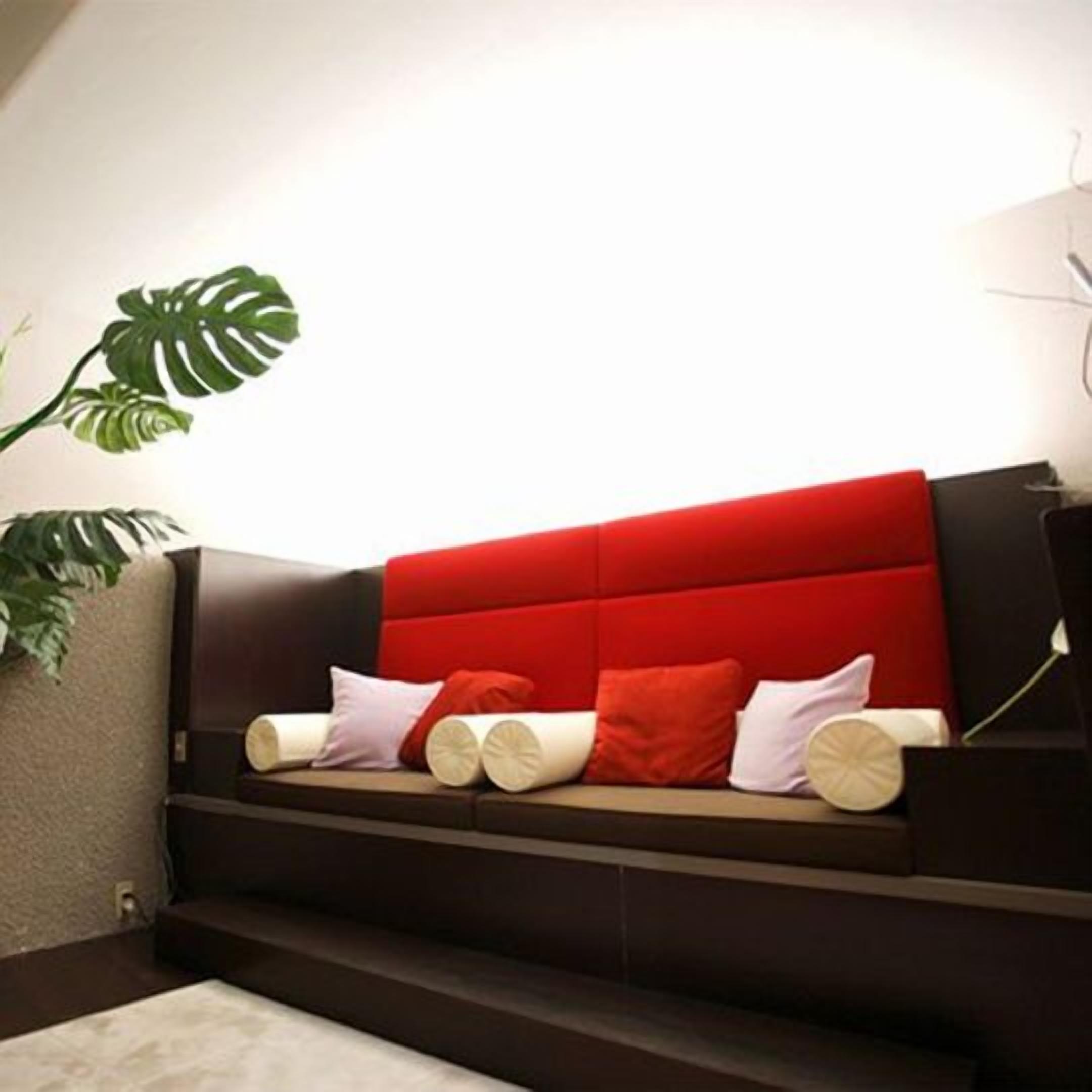 Een moderne woonkamer met een rode bank, een grote groene plant en een trap naar een hoger gelegen verdieping.