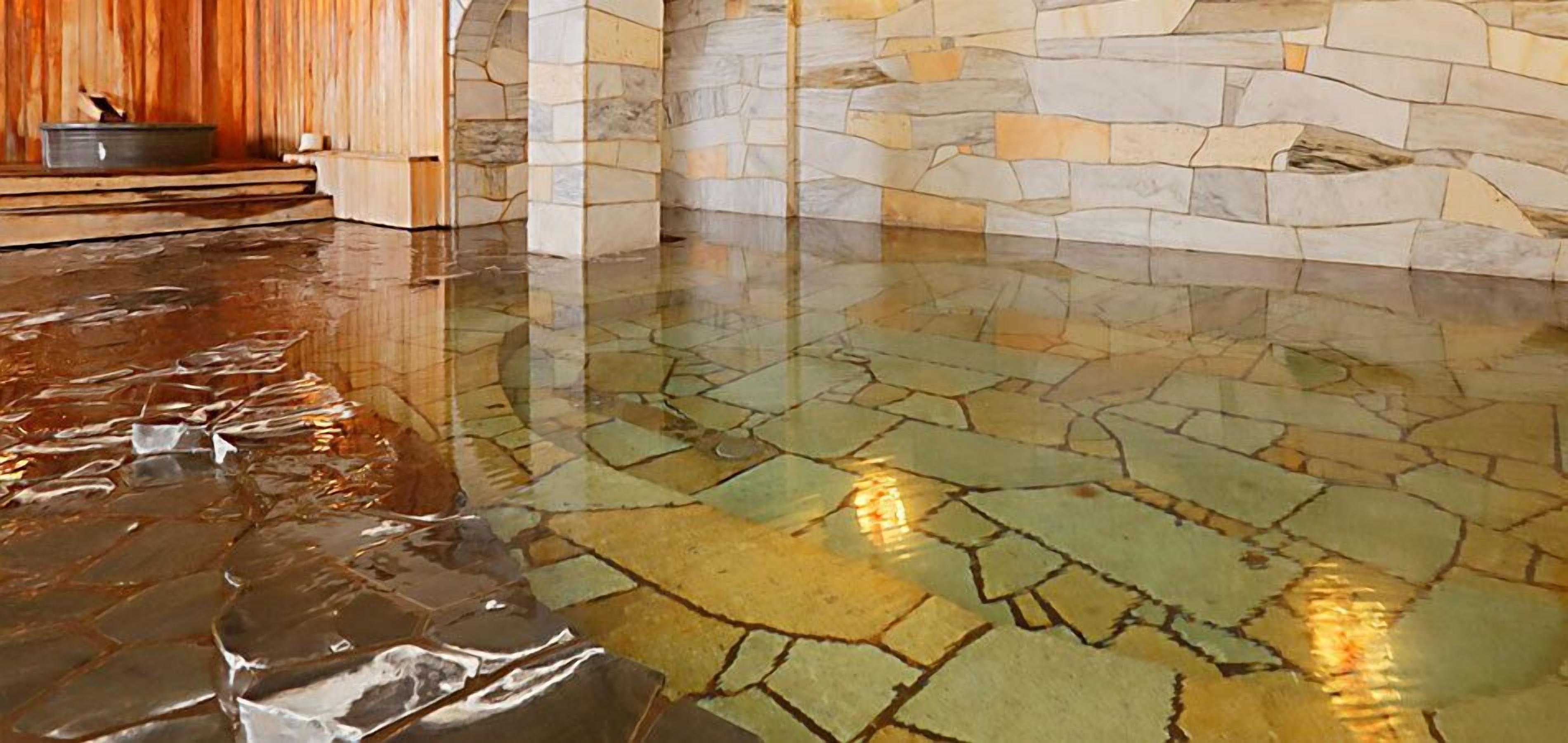 A wet stone floor with a reflective surface, a stone wall, and a wooden panel.