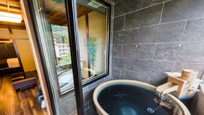 A modern bathroom with a large, round bathtub, a glass shower enclosure, and dark stone walls. - LiVEMAX RESORT KAWAJI (Nikko)