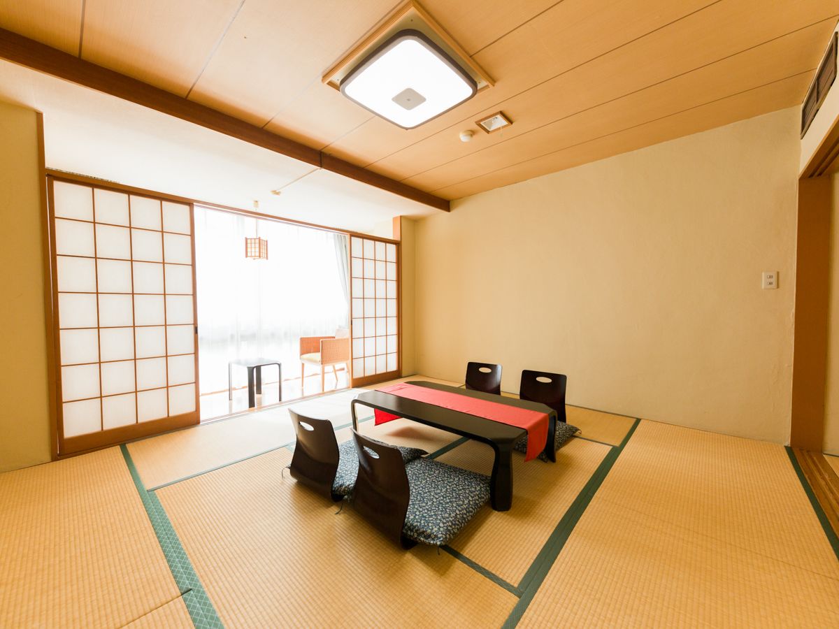 Um espaço com esteiras de tatame, uma mesa baixa, cadeiras e uma porta deslizante.