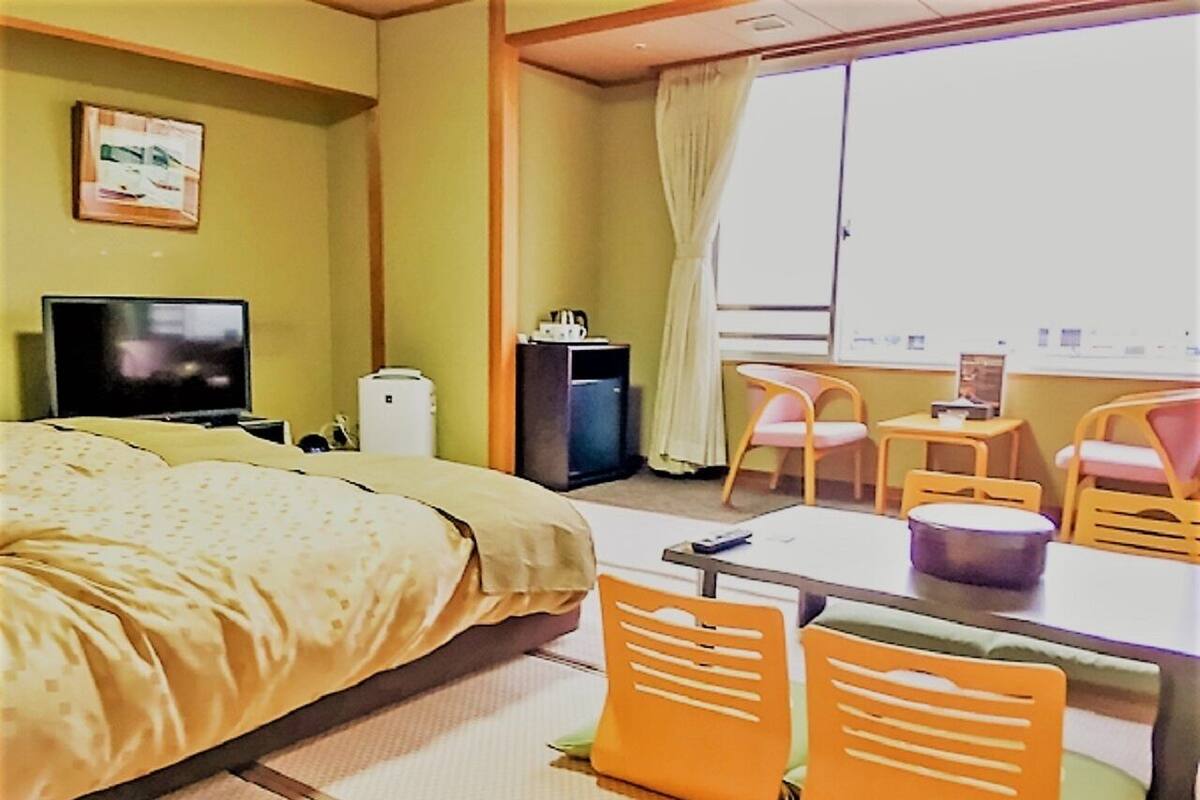 A hotel room with a bed, a desk, a chair, a television, and a window with curtains.