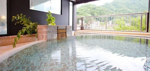 An indoor swimming pool with a clear view of a mountainous landscape through a glass wall.