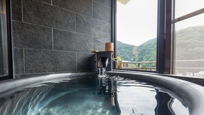 A hot tub with a wooden bucket, water flowing, and a view of a mountainous landscape through a window. - LiVEMAX RESORT KAWAJI (Nikko)