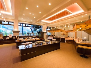 A spacious buffet area with multiple serving stations, a central island, and a seating area with a high ceiling and large windows.