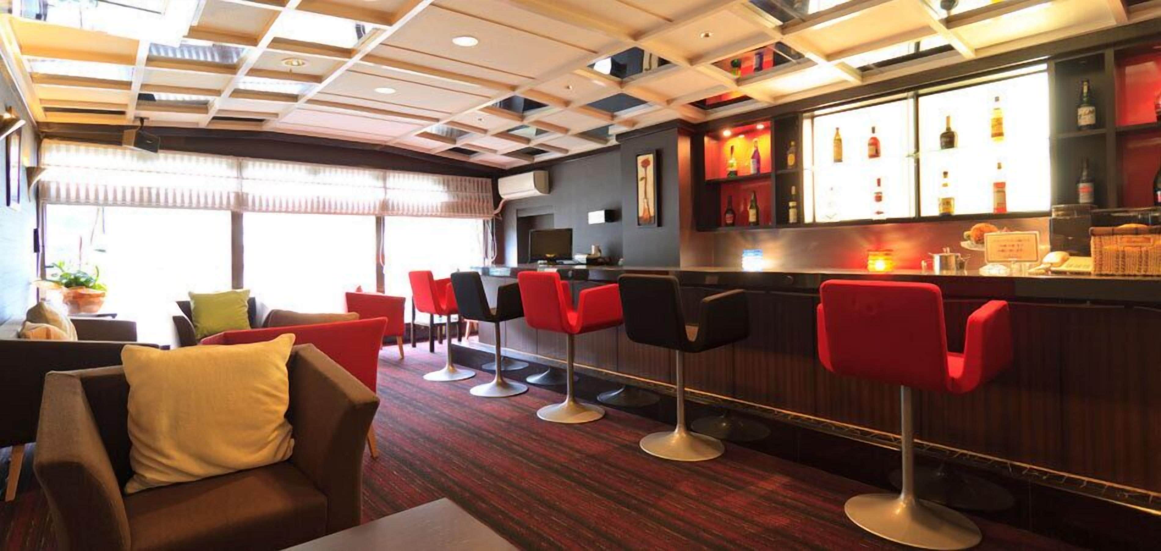 A bar area with red bar stools, a counter with bottles, and a television.