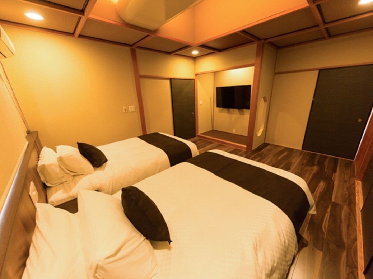 Quarto de hotel com duas camas, piso de madeira, televisão de tela plana e espelho na parede.