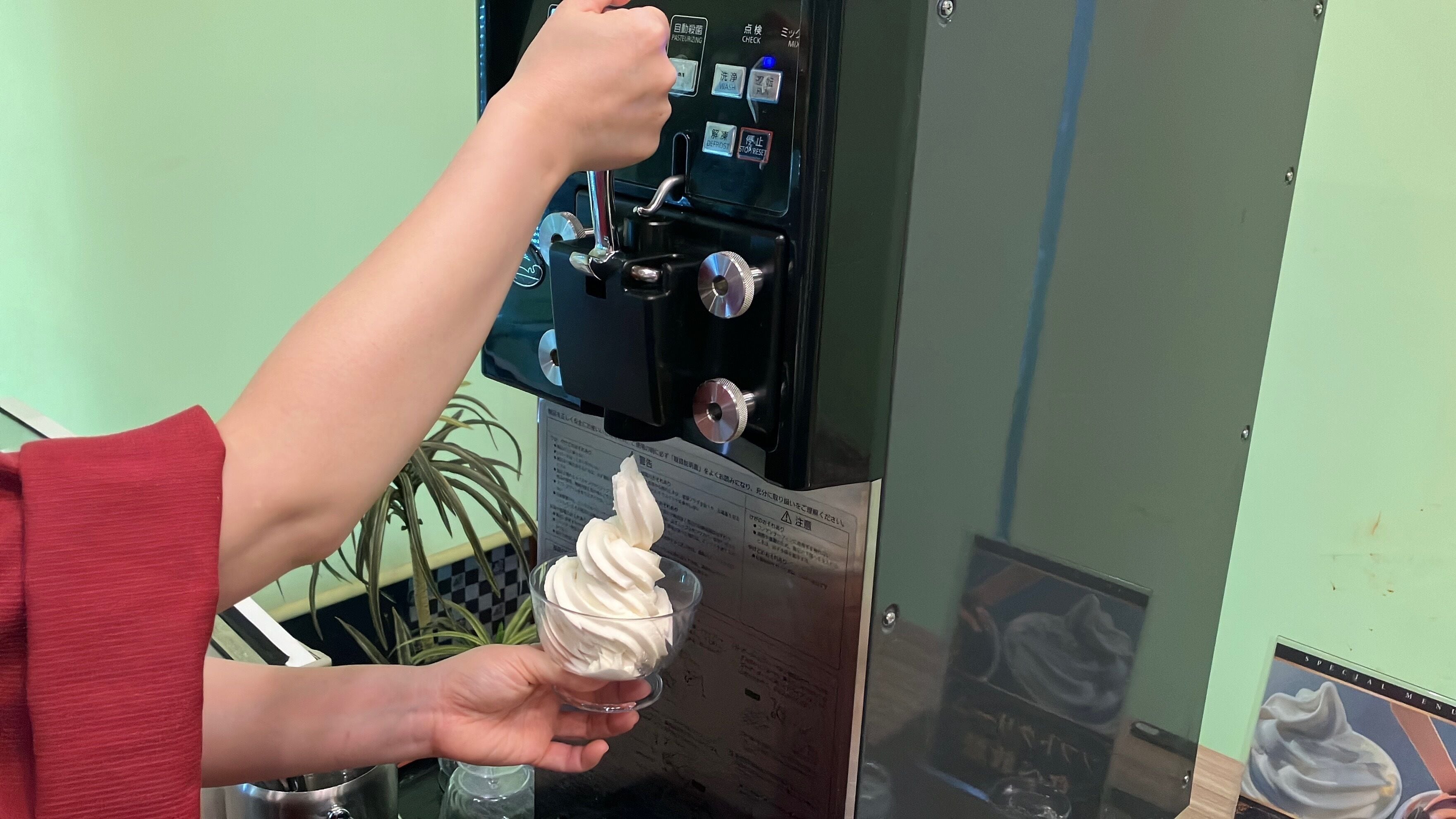 A person holding a glass of ice cream near a vending machine with multiple buttons and a display.