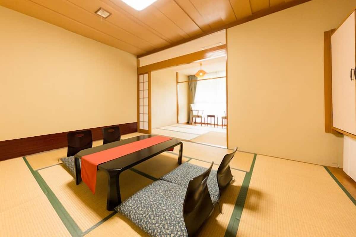 Ein Raum mit Tatami-Matten, einem niedrigen Tisch, Stühlen und einer verschiebbaren Tür zu einem anderen Raum.