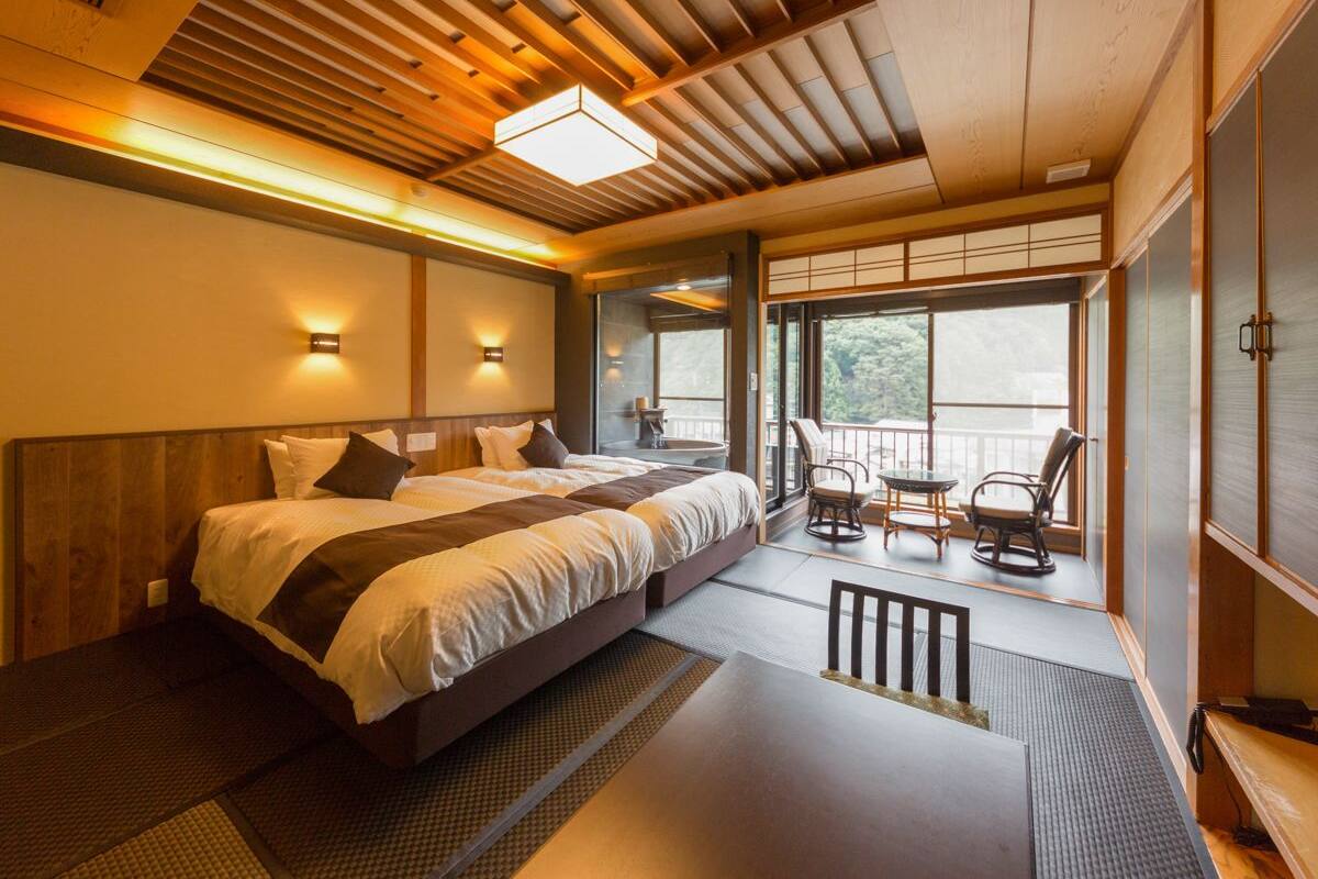 A hotel room with a large bed, a balcony with chairs, and a view of the outdoors.