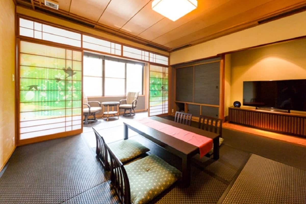 A traditional Japanese-style room with tatami flooring, a low table with cushions, and sliding doors with a view of greenery.