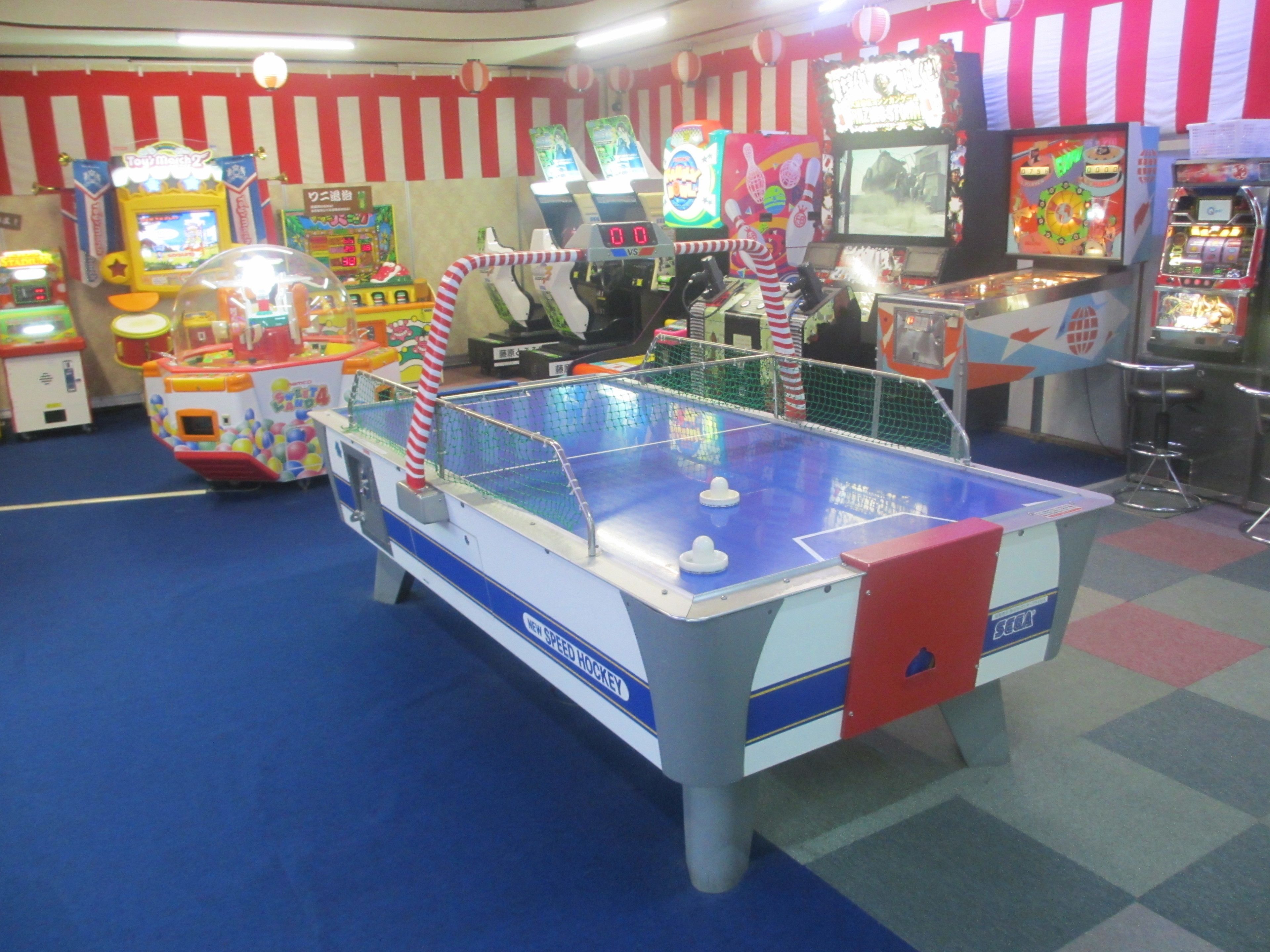 Een snelheidhockeytafel in een vrolijk ingerichte speelhal met diverse spelautomaten op de achtergrond.