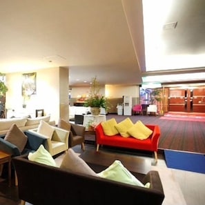 A hotel lobby with multiple seating areas, including sofas and chairs, a reception desk, and a visible entrance.