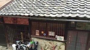 A small building with a tiled roof, a barred window, and a bicycle parked outside. - Guest House Aloes House - Hostel (Onomichi)
