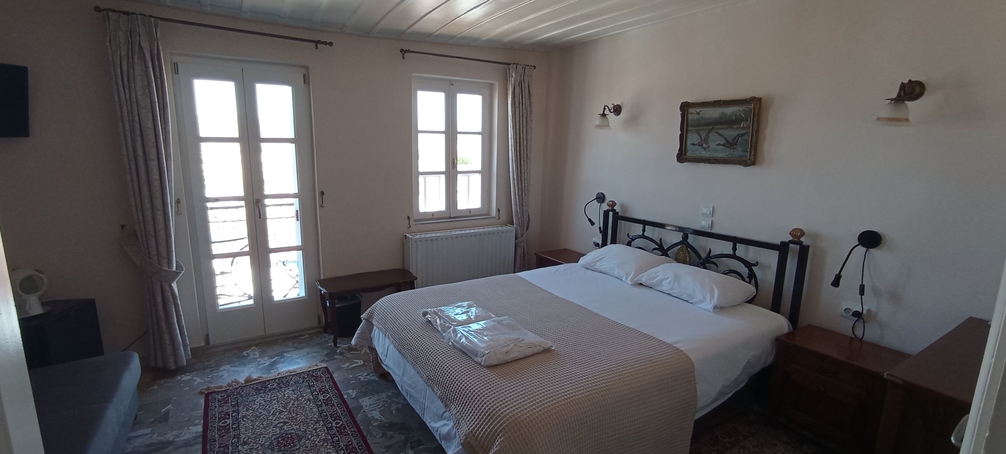 A bedroom with a bed, a nightstand, a dresser, a radiator, and two windows with curtains.