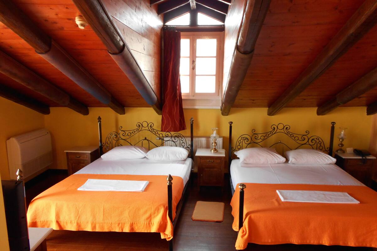 A room with two beds, wooden beams, a window, and a radiator.