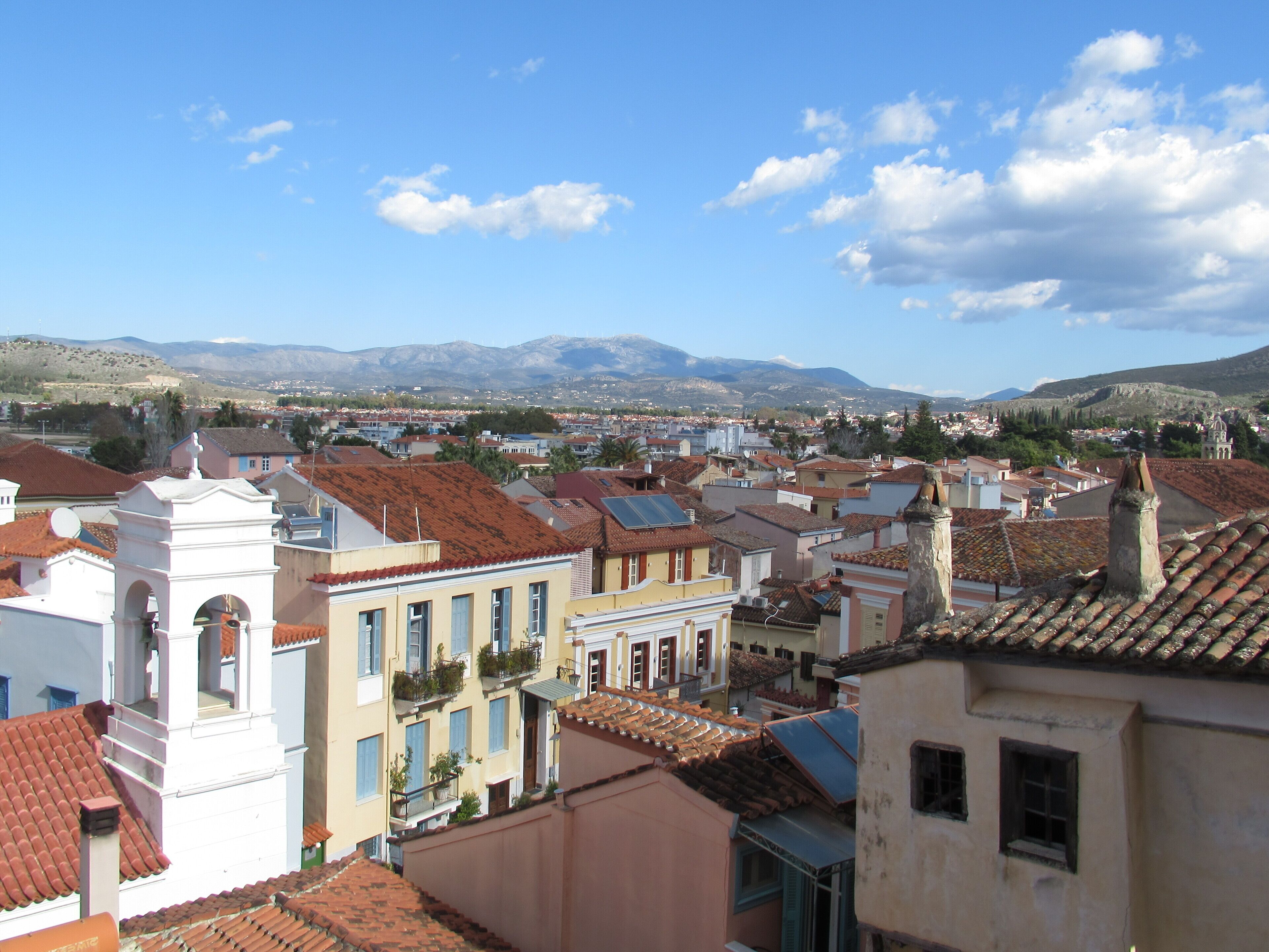 A town with red-tiled roofs, white buildings, and a mountainous backdrop.