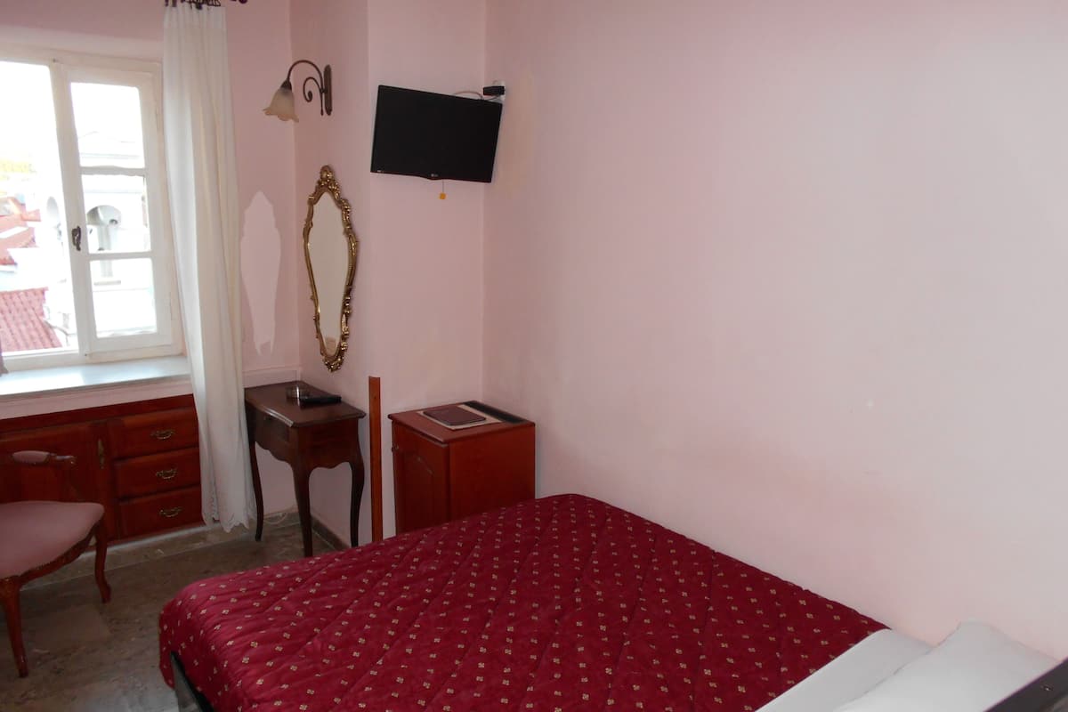 A bedroom with a bed, a desk, a chair, a mirror, and a television on the wall.