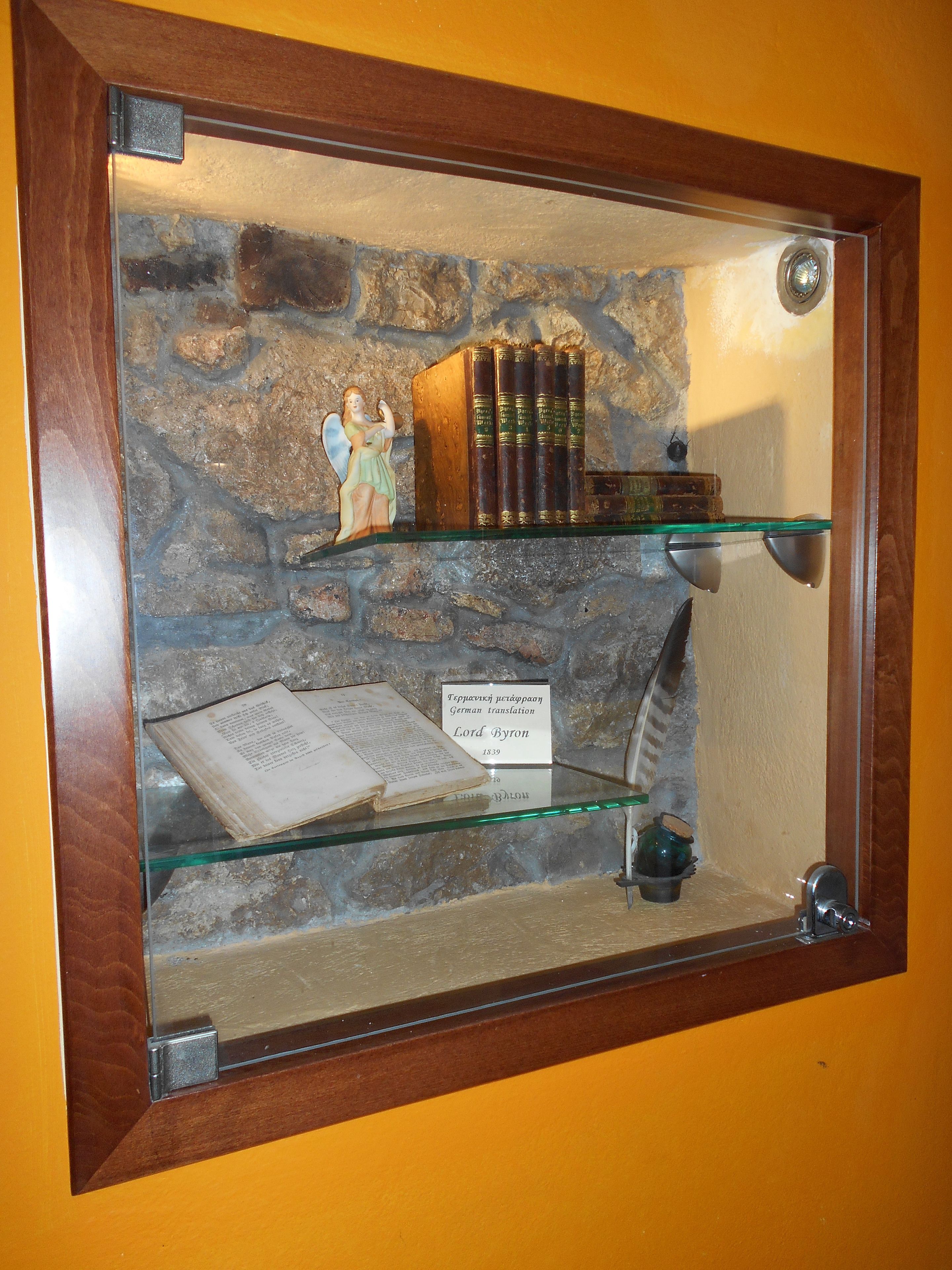 A display case with a stone wall background, featuring a statue, books, and an open book with a label.