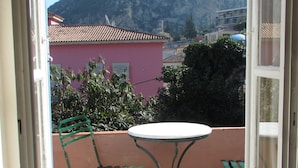 A balcony with a table and chairs, a pink building, and a mountain in the background. - Byron Hotel (Nafplio)