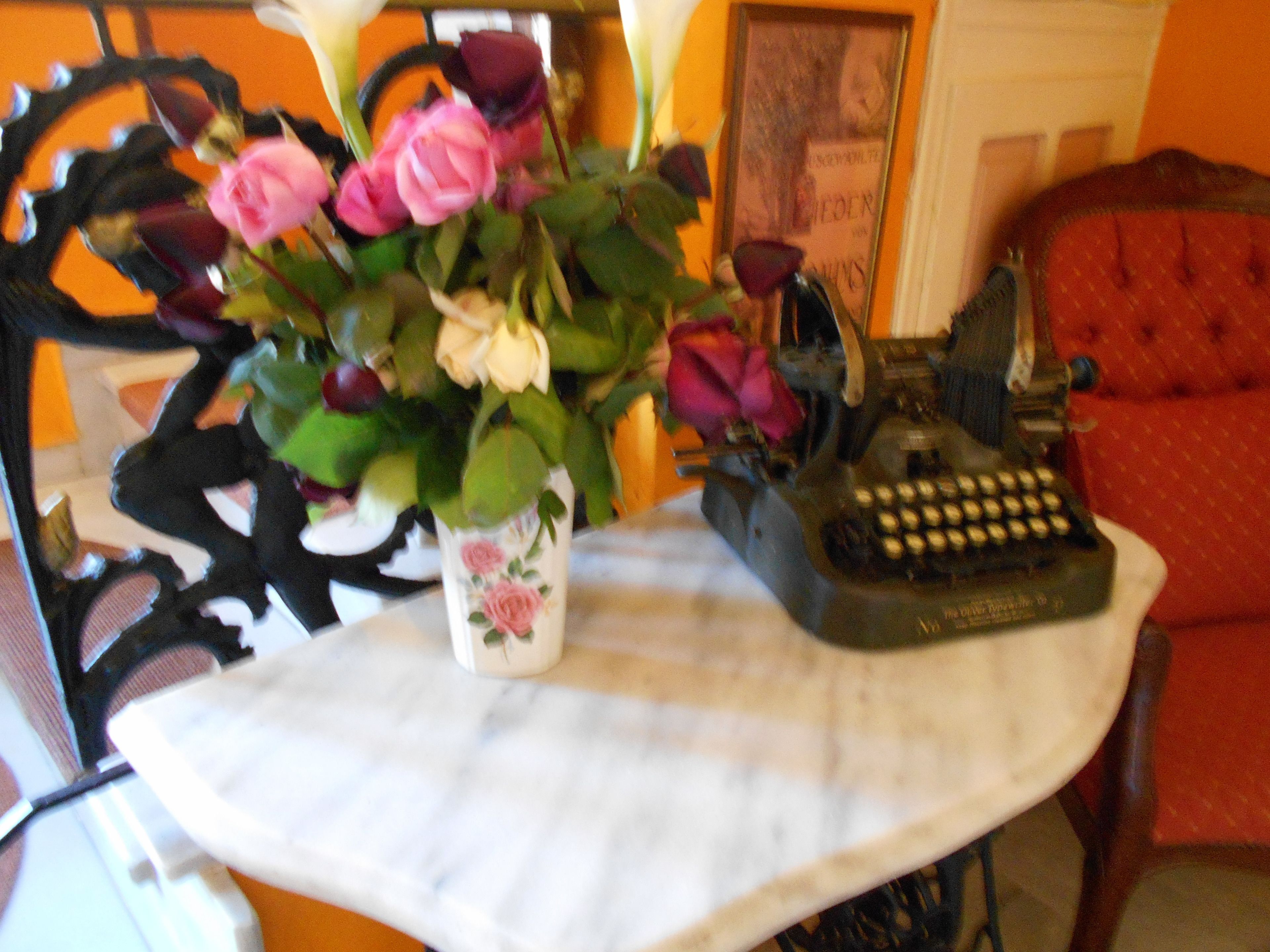 Una mesa con un florero, una máquina de escribir y una silla roja.