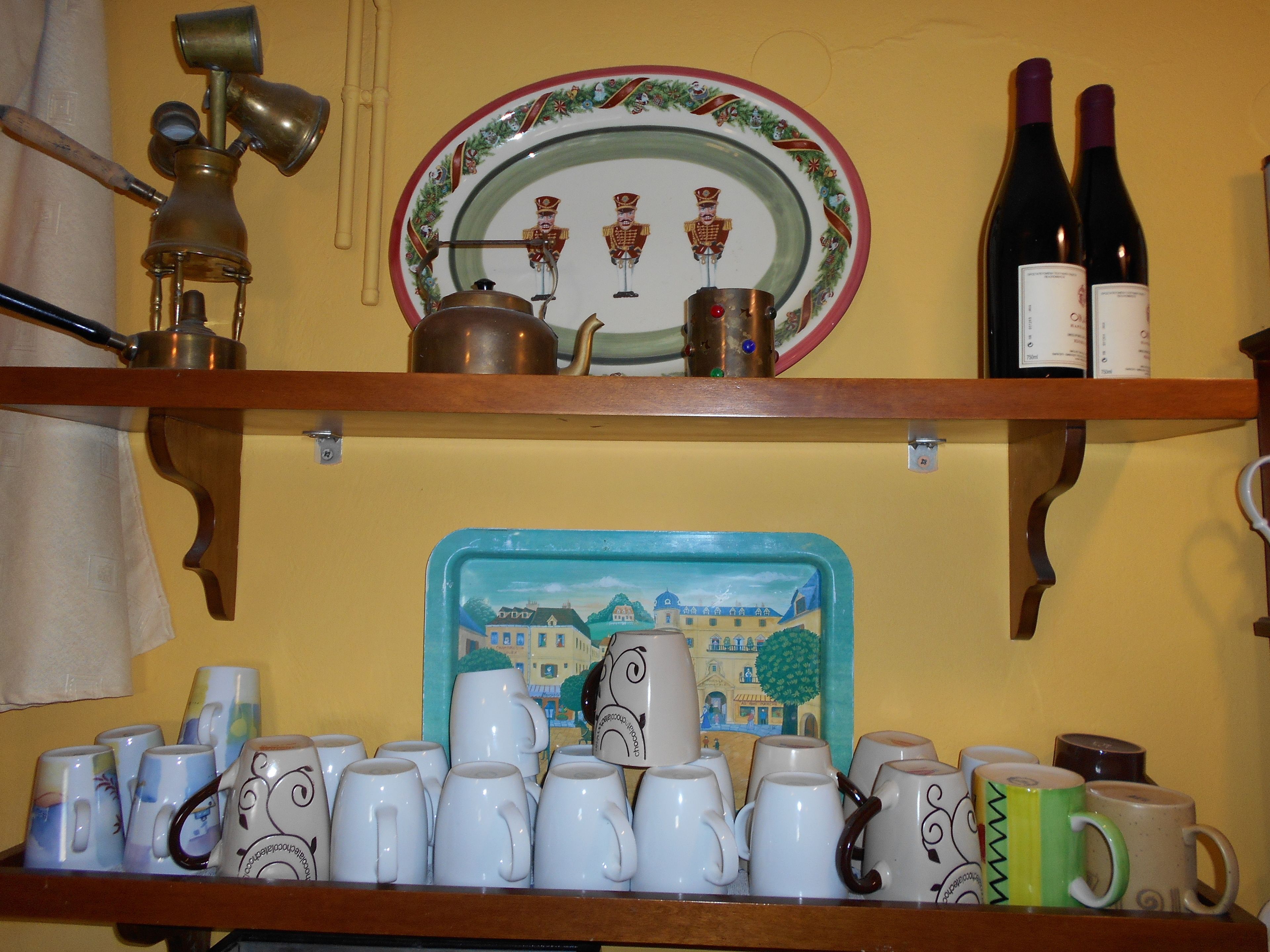 A shelf with various mugs, a plate with nutcracker figures, and two wine bottles.