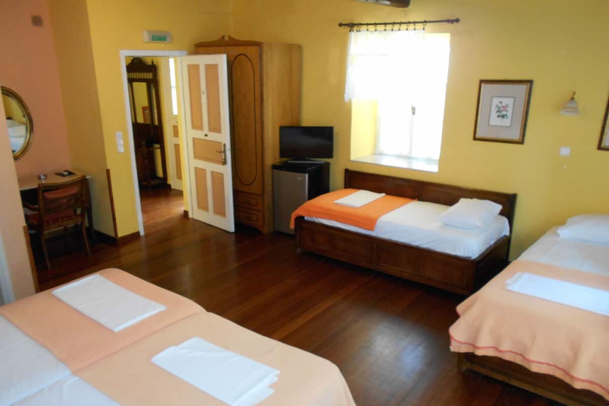 A hotel room with two beds, wooden flooring, a television, and a window with curtains.