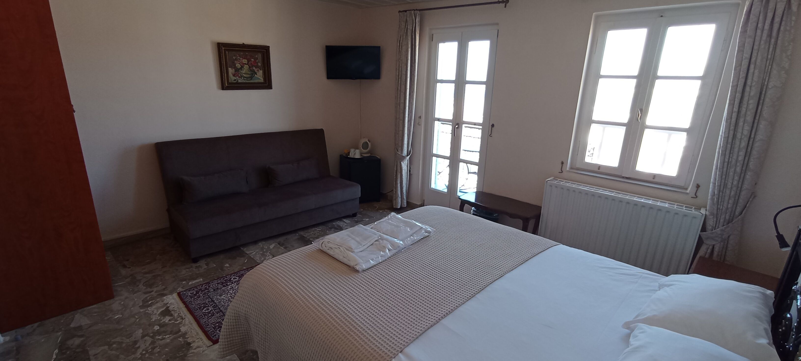 A bedroom with a bed, a sofa, a TV, and a window.