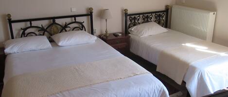 Una habitación con dos camas, cada una con ropa de cama blanca y cabecero. Junto a una cama hay una mesita de noche con una lámpara y un control remoto.