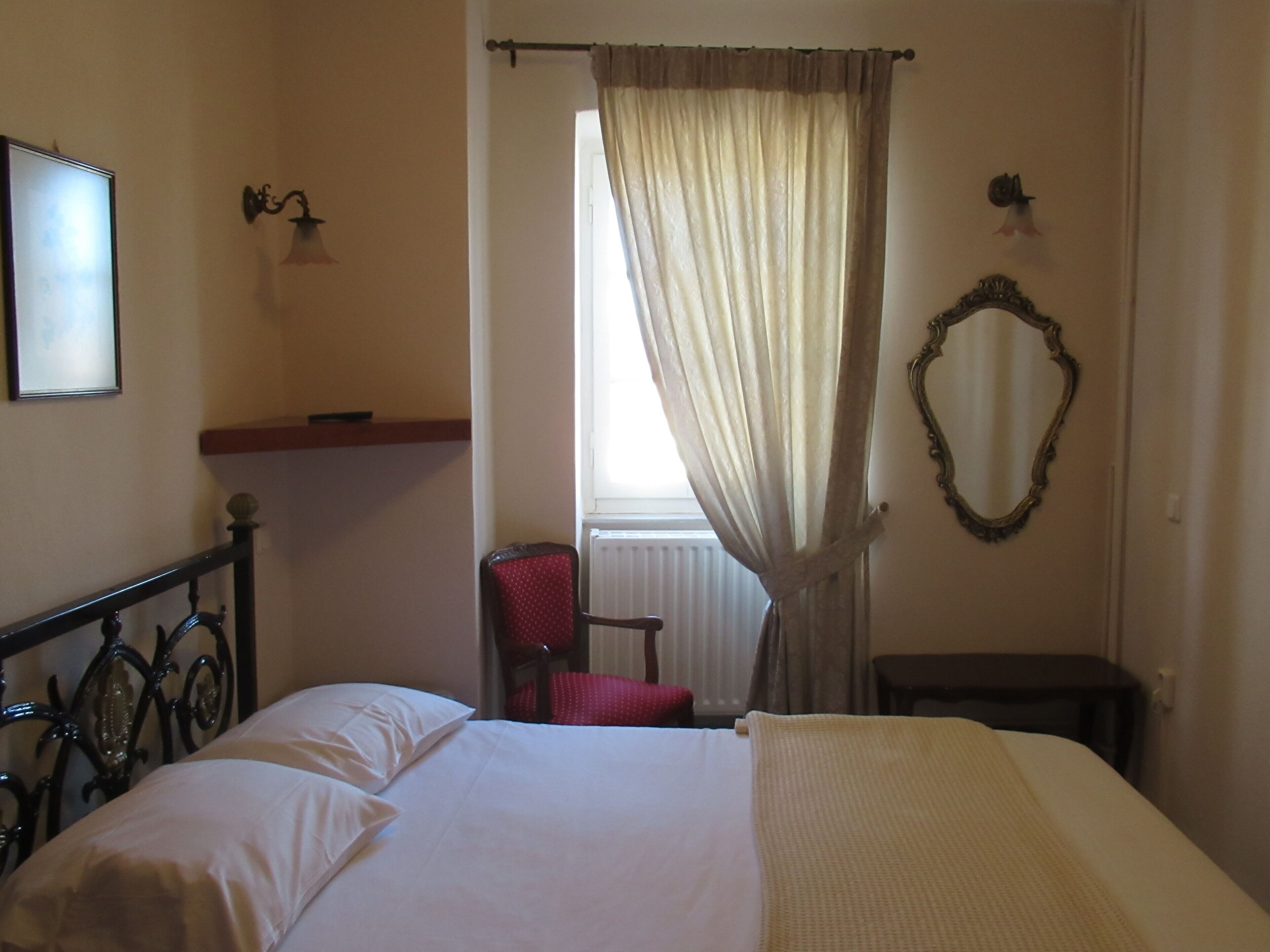 A hotel room with a bed, a chair, a mirror, and a window with curtains.