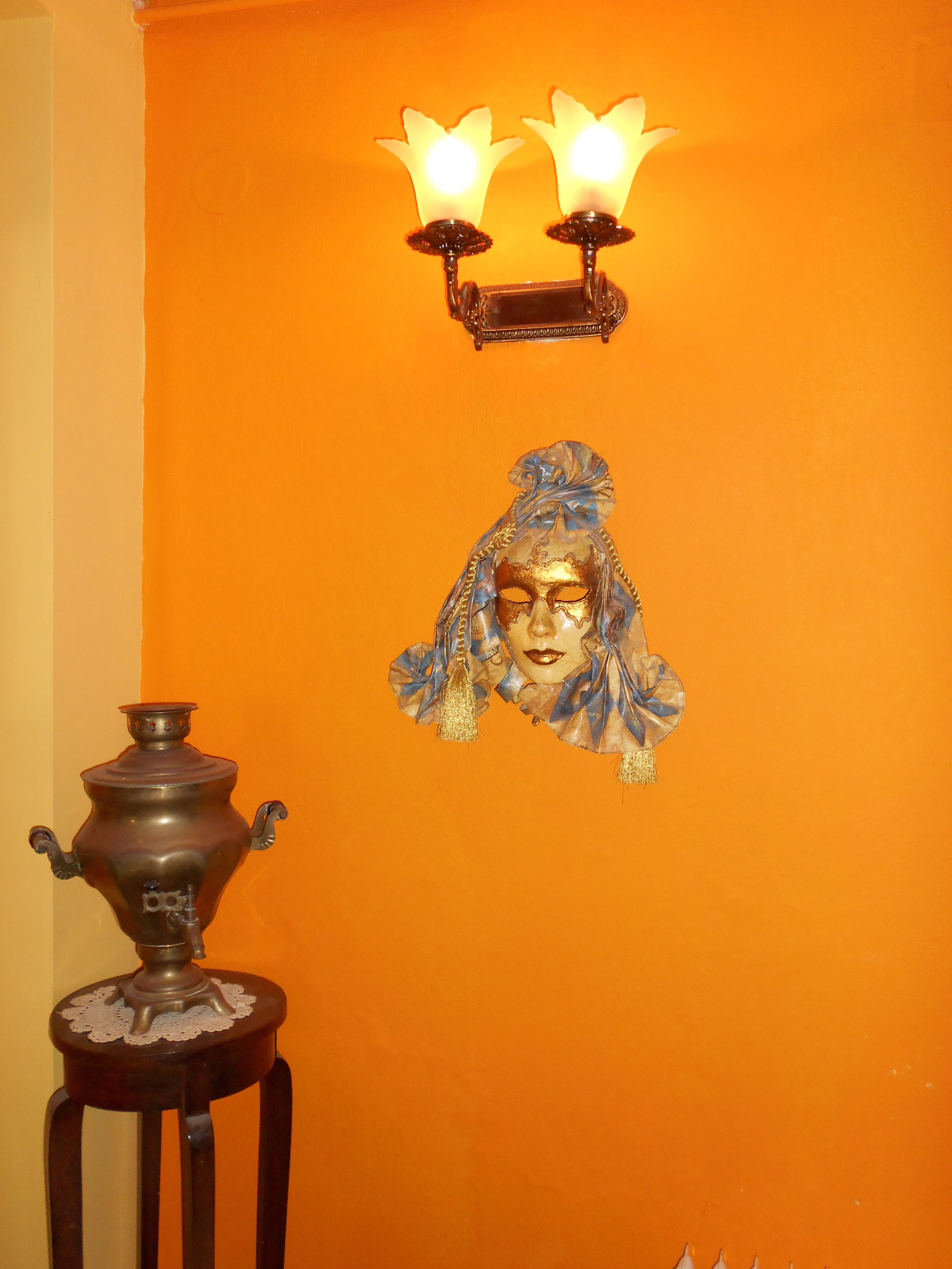 A room with a large orange wall, a decorative lamp with two lights, and a small table with a metal container.