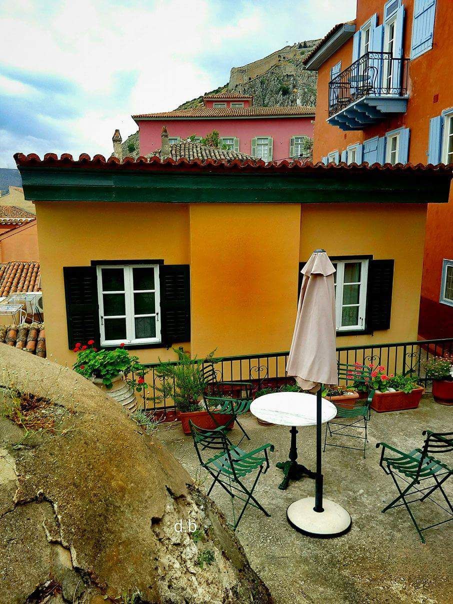 A colorful building with a balcony, outdoor seating, and potted plants.