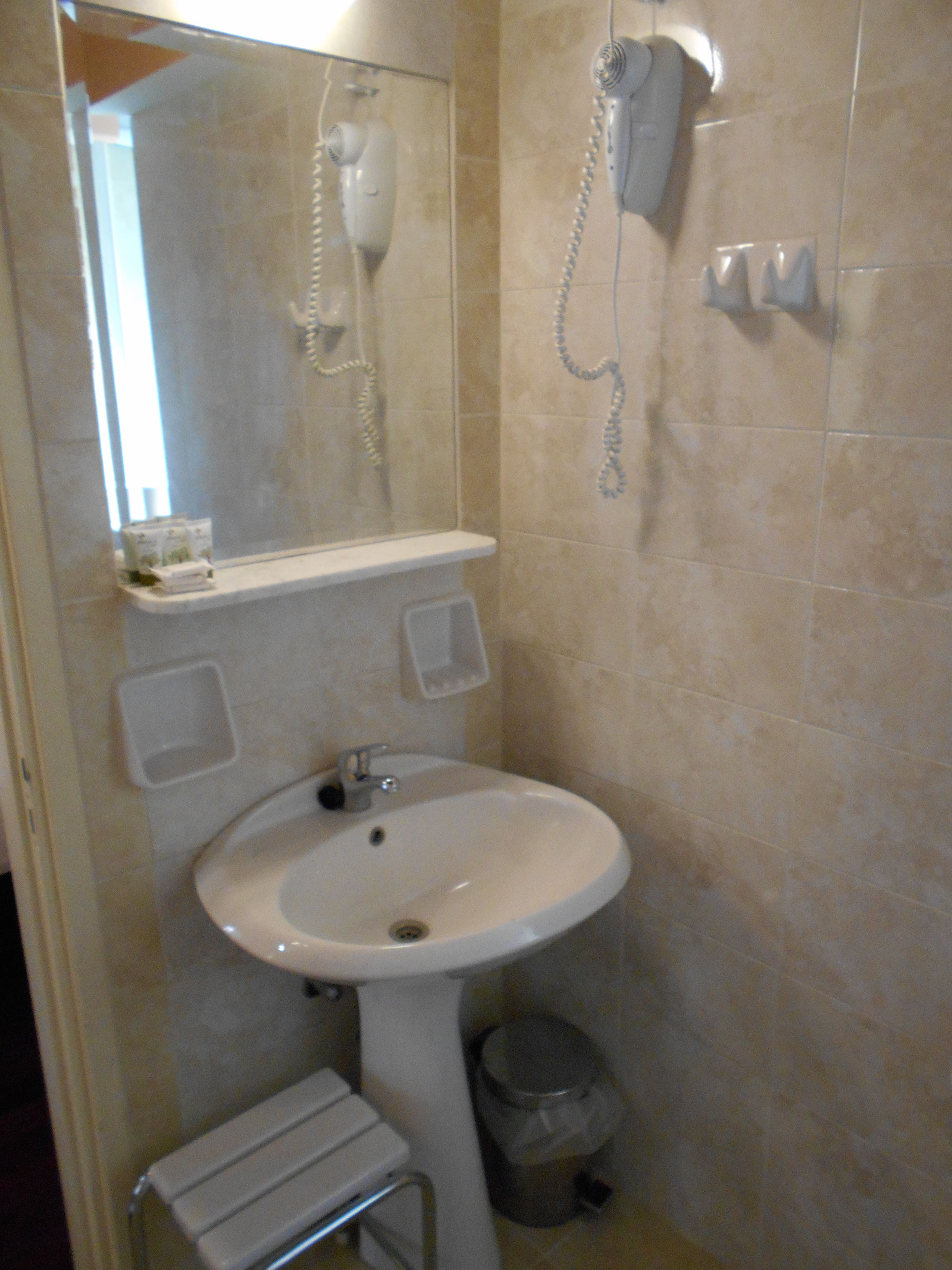 Un baño con lavabo, espejo y secador de pelo fijado a la pared.